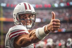 American football player in a white helmet and uniform gives a thumbs up with his right hand. On the background of the arena grandstand photo