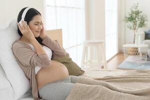 Happy pregnant woman with headphones listening to mozart music and lying on bed, pregnancy concept photo