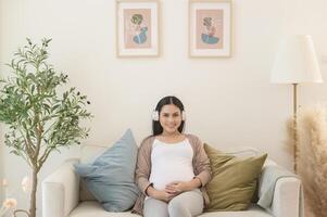 Happy pregnant woman with headphones listening to mozart music and lying on sofa, pregnancy concept photo