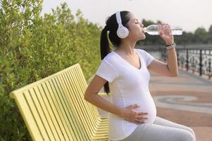 Beautiful pregnant woman drinking bottle of pure water in the park, Healthy and active pregnancy lifestyle concept. photo