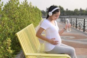 Beautiful pregnant woman drinking bottle of pure water in the park, Healthy and active pregnancy lifestyle concept. photo