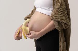 retrato de hermosa embarazada mujer participación plátano terminado blanco antecedentes estudio, salud y maternidad concepto foto