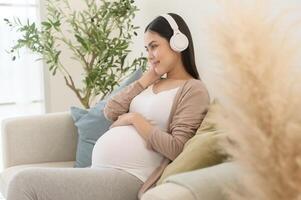 contento embarazada mujer con auriculares escuchando a mozart música y acostado en sofá, el embarazo concepto foto