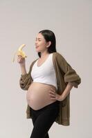 Portrait of Beautiful pregnant woman holding banana over white background studio, health and maternity concept photo