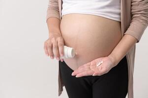 retrato de hermosa embarazada mujer tomando píldora y vitamina terminado blanco antecedentes estudio, salud y maternidad concepto foto