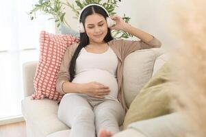 Happy pregnant woman with headphones listening to mozart music and lying on sofa, pregnancy concept photo