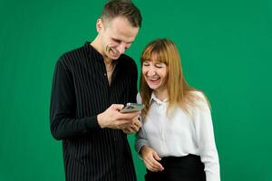 man and woman with gadgets tablet phone in hands on green background talking laugh holding meeting learning to work on Internet flirting relationships flirting couple solving issue positive emotions photo