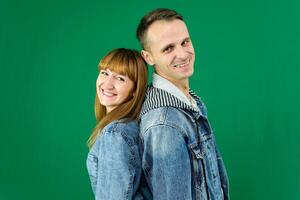 Young cheerful couple smiling, hugging, wearing, Stand with your backs to each other, denim clothes on a green background photo