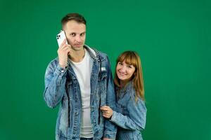 Cheerful guy and girl in denim clothes, couple, family. guy calling on the phone on a green background photo