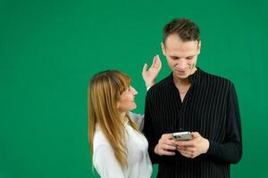 man and woman with gadgets tablet phone in hands on green background talking laugh holding meeting learning to work on Internet flirting relationships flirting couple solving issue positive emotions photo