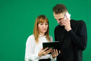man and woman with gadgets tablet phone in hands on green background talking laugh holding meeting learning to work on Internet flirting relationships flirting couple solving issue positive emotions photo