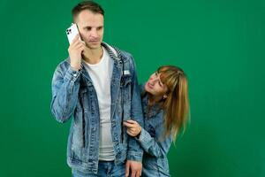 Cheerful guy and girl in denim clothes, couple, family. guy calling on the phone on a green background photo