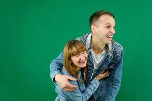 Young cheerful couple smiling, hugging, wearing, Looking away, denim clothes on a green background photo