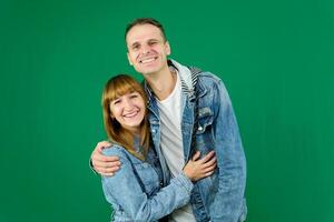 Young cheerful couple smiling, hugging, wearing denim clothes on a green background photo