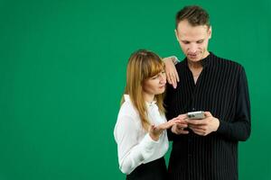 man and woman with gadgets tablet phone in hands on green background talking laugh holding meeting learning to work on Internet flirting relationships flirting couple solving issue positive emotions photo