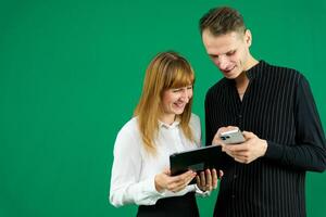 man and woman with gadgets tablet phone in hands on green background talking laugh holding meeting learning to work on Internet flirting relationships flirting couple solving issue positive emotions photo