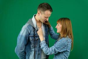 galanteo, un hombre y un mujer en mezclilla trajes en un verde fondo, croma, ajustando camisa, en pie para foto, posando en el estudio, hombre, abusador, demostración cómo a comportarse, sonriente, riendo agradablemente foto