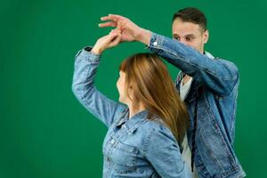 dance bachata on a green background chromakey man and woman in denim clothes dance a movement Latin American dance smile spend time together entertainment hobby take care of health studio exercise photo