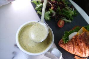 delicioso bebida matcha espuma con un cuchara cucharón arriba sano verde té con leche. sano comiendo cuerno con queso y ensalada francés desayuno almuerzo bocadillo cena dieta delicioso foto