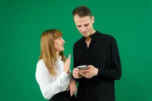 man and woman with gadgets tablet phone in hands on green background talking laugh holding meeting learning to work on Internet flirting relationships flirting couple solving issue positive emotions photo