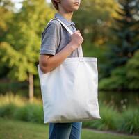 Tote bag mockup. Boy carrying reusable white cotton linen eco organic fabric canvas blank totebag with natural green leaves trees background. photo