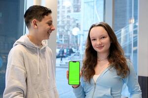 Glad young european, asian and arabic people point finger at smartphone with empty screen, make gesture ok and thumb up approve website, device, app isolated on yellow background, studio panorama photo