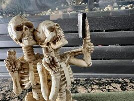 Halloween decorations joke Skeletons without legs take a selfie look at a mobile phone they smile with all their teeth and show two fingers up as if Victor place for text on background of fireplace photo