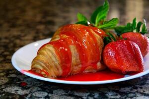 Pouring strawberry syrup on sweet croissants on white plate. Delicious croissants for breakfast or snack photo