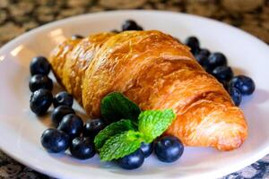 Extreme close up powdered sugar is poured onto croissants with blueberry. strainer with flour or sugar, which is sprinkled with baked goods before serving. Breakfast or dessert cooking concept photo