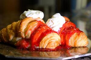 Pouring strawberry syrup on sweet croissants on white plate. Delicious croissants for breakfast or snack photo