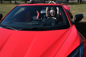 lujoso coche y niña un niña se sienta detrás el rueda de un rojo coche con su manos arriba, disfruta vida, un Rico vida, un lote de dinero. foto