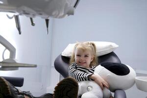 beautiful little blond blonde girl in dentist office big shoes on feet close-up latest technology soft toy in hands smile meeting the doctor alone in the frame slow slow motion camera zooms in and out photo