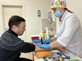 Close up of nurse disinfecting male arm before blood test. Man is sitting on chair near medical set Skillful general practitioner testing male blood photo