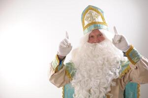 white rich beard and golden blue suit of St. Nicholas raised two fingers up listen to me look here attention Sinterklaas portrait positive emotions Dutch Santa Claus St Nicholas christmas new year photo