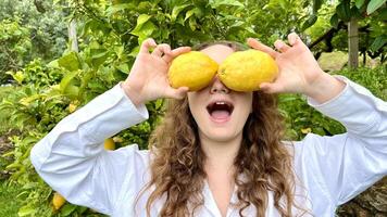 girl teenager have fun dancing smiles and laughs against the backdrop of a lemon tree in her hands she has lemons she fools around with them photo