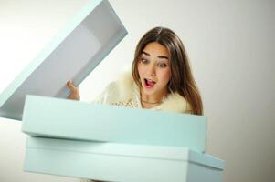 New Year's gift for Christmas A young woman in a white blouse with fur on a white background near the box received a delivery Studio shooting on a white background blue boxes girl is happy and joyful photo