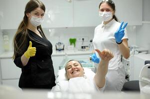 dental office satisfied patient showing thumbs up big class she liked service new technology doctor and assistant dentist in black teeth put filling put plaque stones prosthetics root canal treatment photo