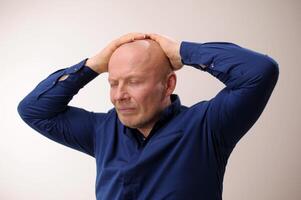 Need medicine for migraine Headache man put his hands on his head and closed his eyes an unpleasant sensation Emotions of an adult handsome bald man A man on a white background in a blue shirt photo