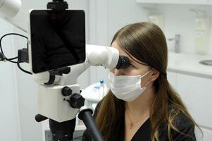 grande pantalla tableta joven dentista se sienta cerca microscopio calipso escáner investigación prótesis relleno canales dientes largo pelo negro vestir código blanco antecedentes último tecnología equipo microscopio foto