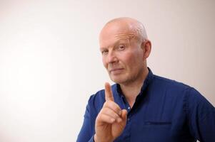 Strict boss Attention Emotions of an adult handsome bald man A man on a white background in a blue shirt family rules man raised thumbs up showing that It will be as he said at work and at home photo