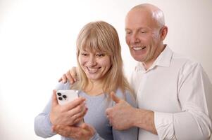 Happy retired family couple using mobile phone for call together, talking to relations, getting good news, having fun, smiling and laughing. Carefree mature pensioners chatting online on cell photo