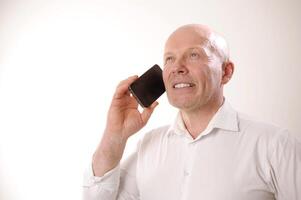 male pensioner looks up he holds phone pleasantly expects winning hope yes opportunities for salary increase white studio shirt there is space for text portrait of an adult male confident bald no hair photo