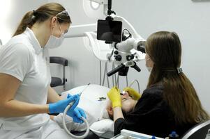 Calipso scanner dental newest office new equipment prosthetics canals fillings Medium shot of female dentist in black coat, mask and gloves using dental microscope to examine patients teeth photo