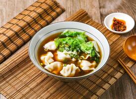 Beef dumplings soup with chilli sauce, spring onion, wooden spoon, and chopsticks served in dish isolated on mat side view of taiwanese food photo