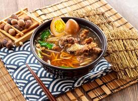 Pork Ribs Crispy Noodles soup with preserved egg, chopsticks served in dish isolated on napkin side view on table taiwan food photo