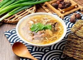 Ancient style mushroom meat soup with noodles, spring onion, spoon and chopsticks served in bowl isolated on napkin side view on table taiwan food photo