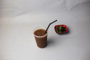 Tetul Juice or Tamarind water with straw served in disposable glass isolated on grey background side view of healthy organic drink photo