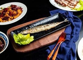 Grilled saury fish with lemon and lettuce spoon and fork served in dish isolated on wooden board side view of taiwan food photo