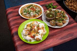 Spicy Chotpoti, plain or Doi Fuchka, pan puri, or gol gappa filled with herbs with spicy water served in plate isolated on wooden table side view of bangladeshi street food photo