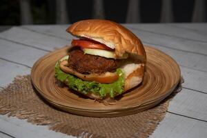 Classic Beef burger with tomato, lettuce and cucumber served in dish isolated on napkin bangladeshi food side view on table photo